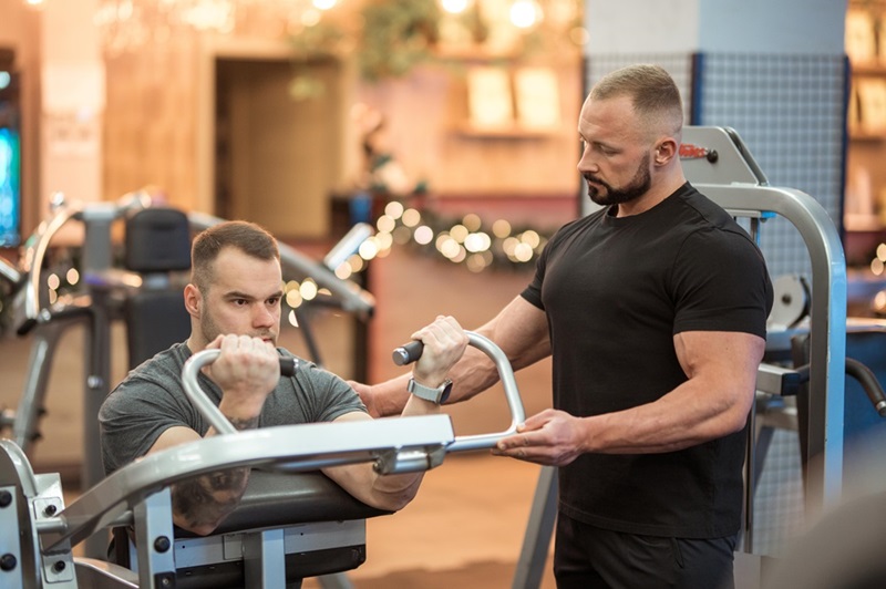 Mezczyna trenuje bicepsy pod okiem trenera personalnego